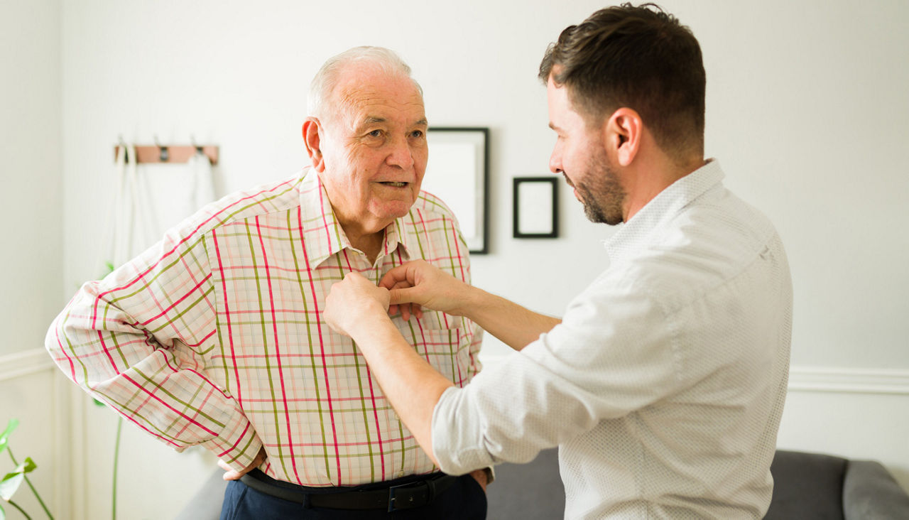 Young man buttoning the shirt of his father or grandfather