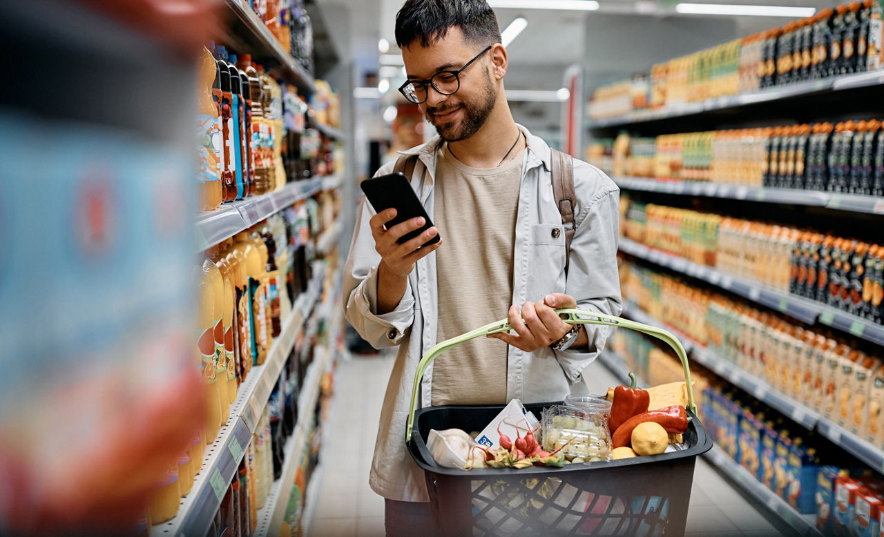 Young man using cell phone while shopping in supermarket. 