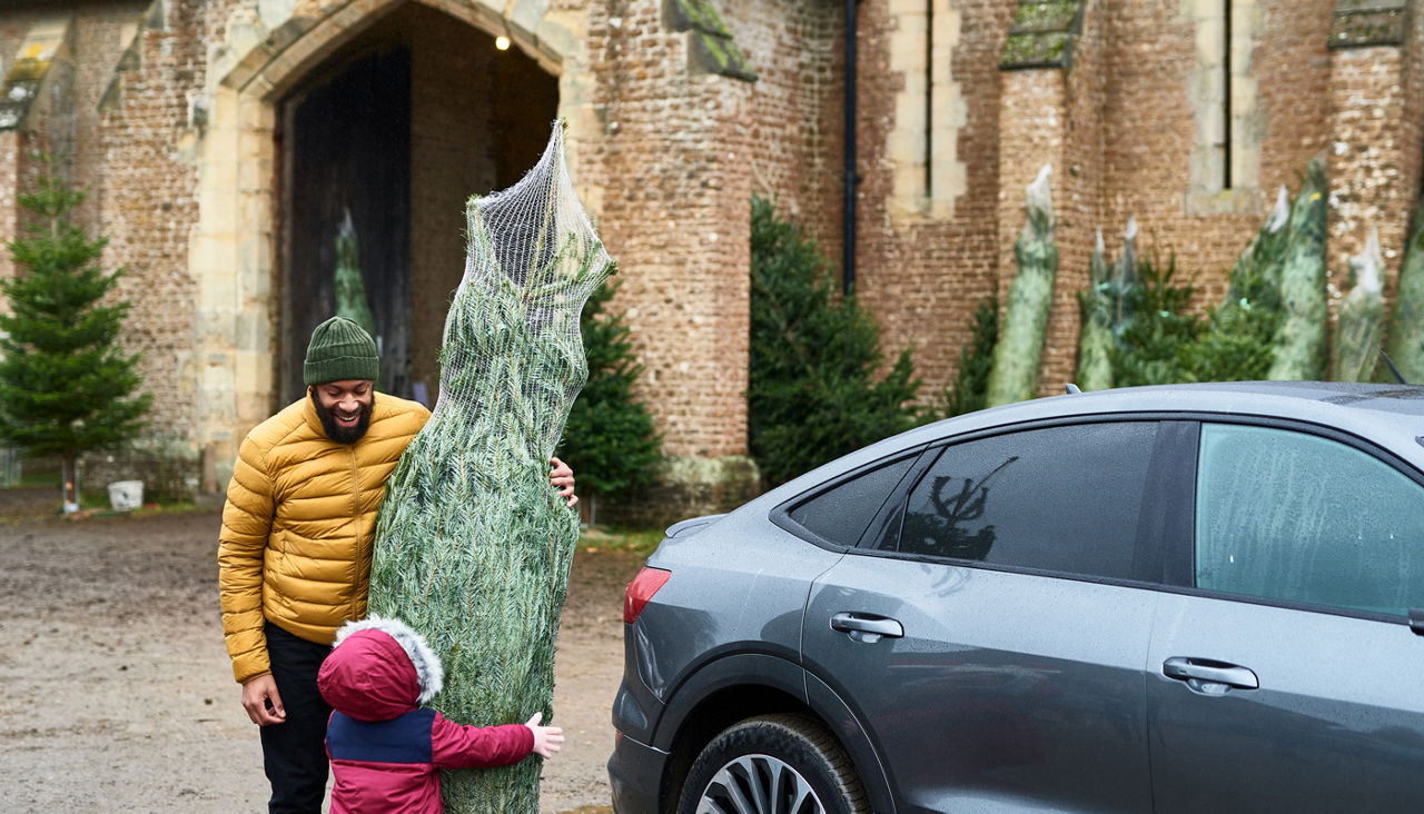 father and young daughter about to put Christmas tree they've bought into their car