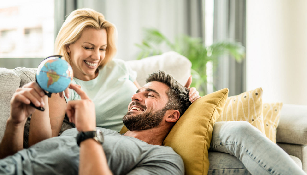Couple lounging on couch looking at a mini globe of the world deciding where to travel