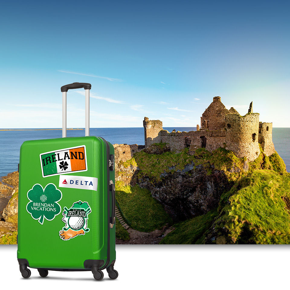Green suitcase with Ireland stickers stands in front of a Ireland castle background image. 