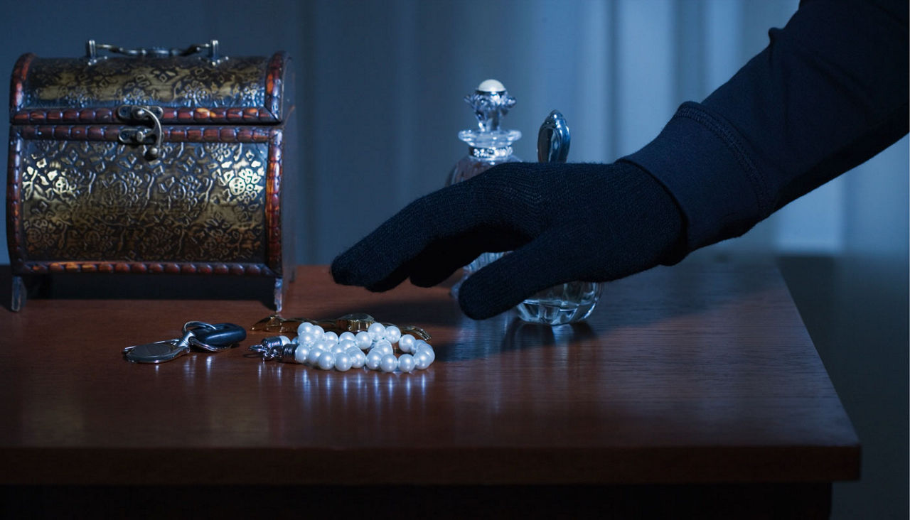 hand with black glove shown stealing jewelry from a dresser