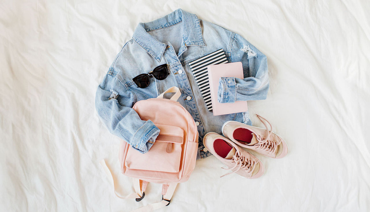 Blue jean jacket pale pink with backpack, book and sneakers on white. Women's stylish autumn or spring outfit. Trendy clothes for college. Back to school concept.  Flat lay, top view.