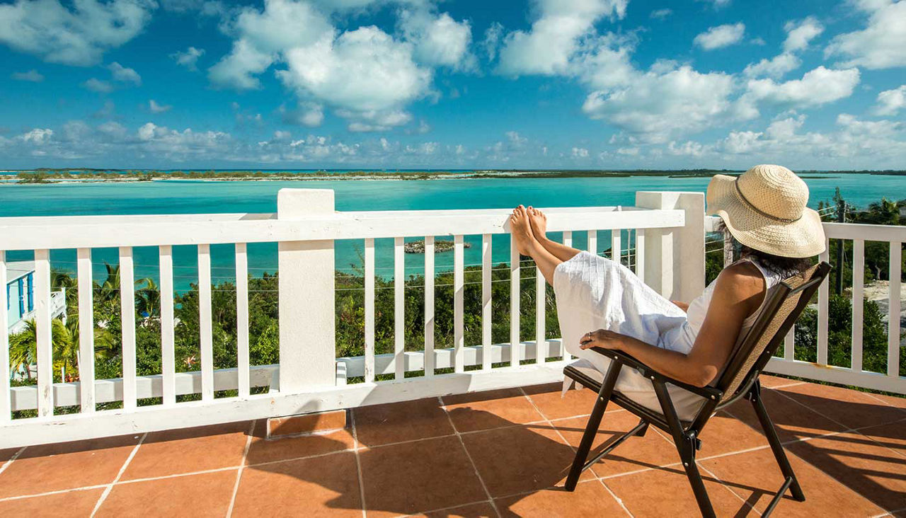 Woman wearing a sun hat relaxing on a chair on a balcony in the Bahamas, view of the ocean