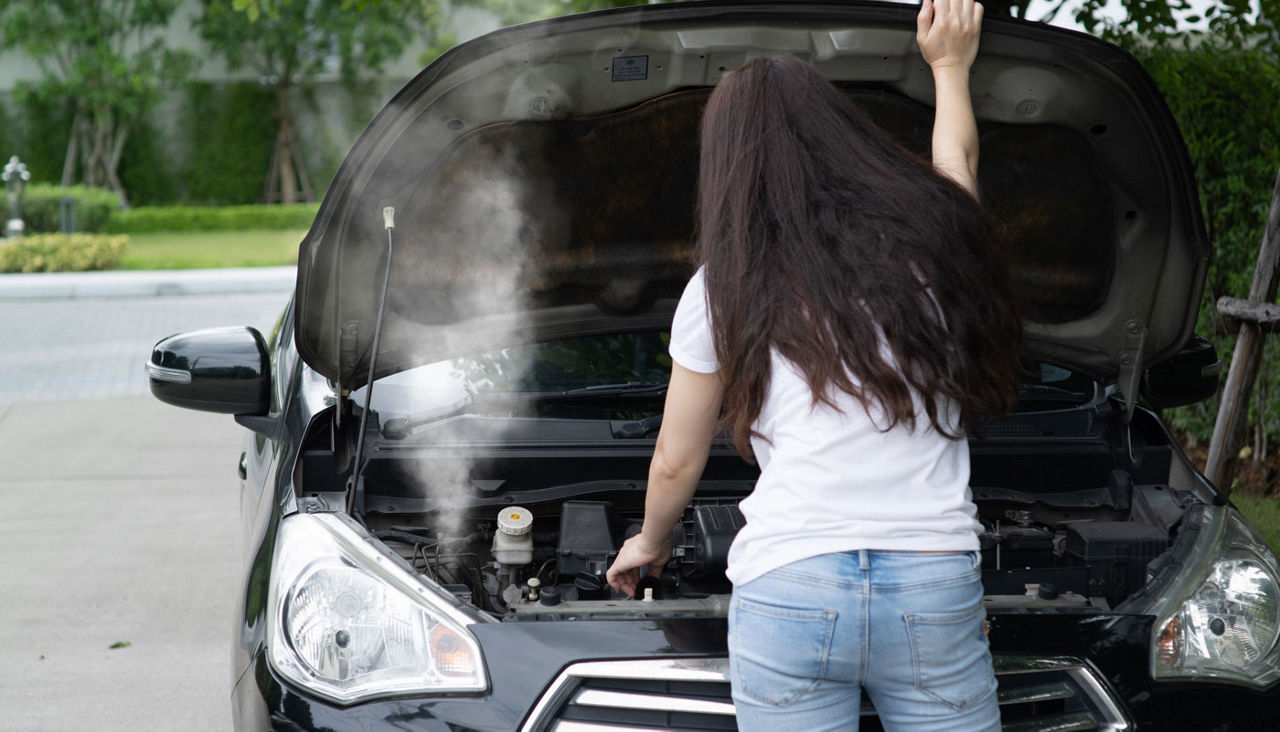 A woman opens the car hood, car breaks down on the side of the road, smoke from the engine.