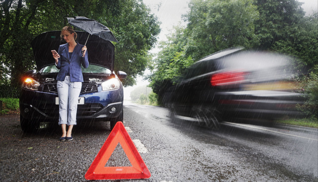 A woman standing near her car in the rain with the hood up as she calls for assistance.