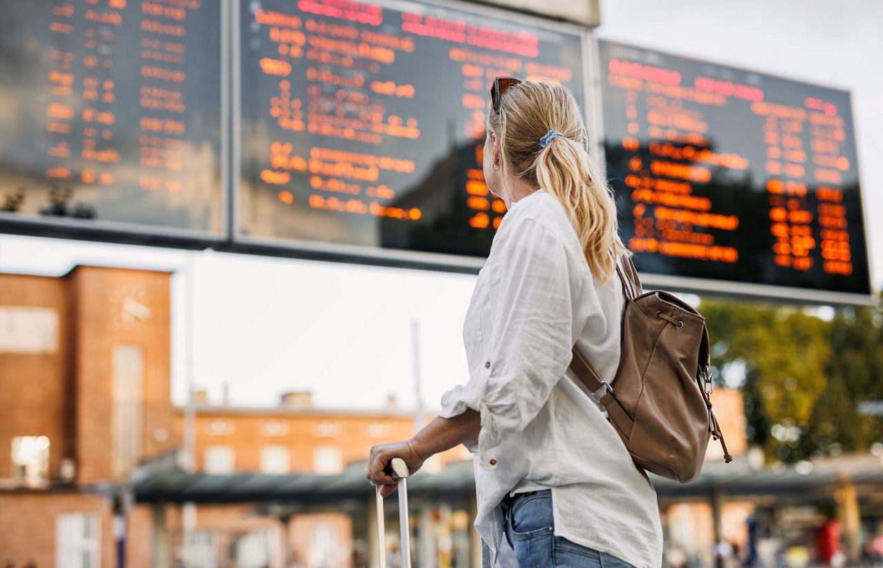 Woman passenger is checking arrival and departure board schedule timetable at airport