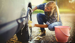 A young woman kneeling down as she scrubs the tire of a car.