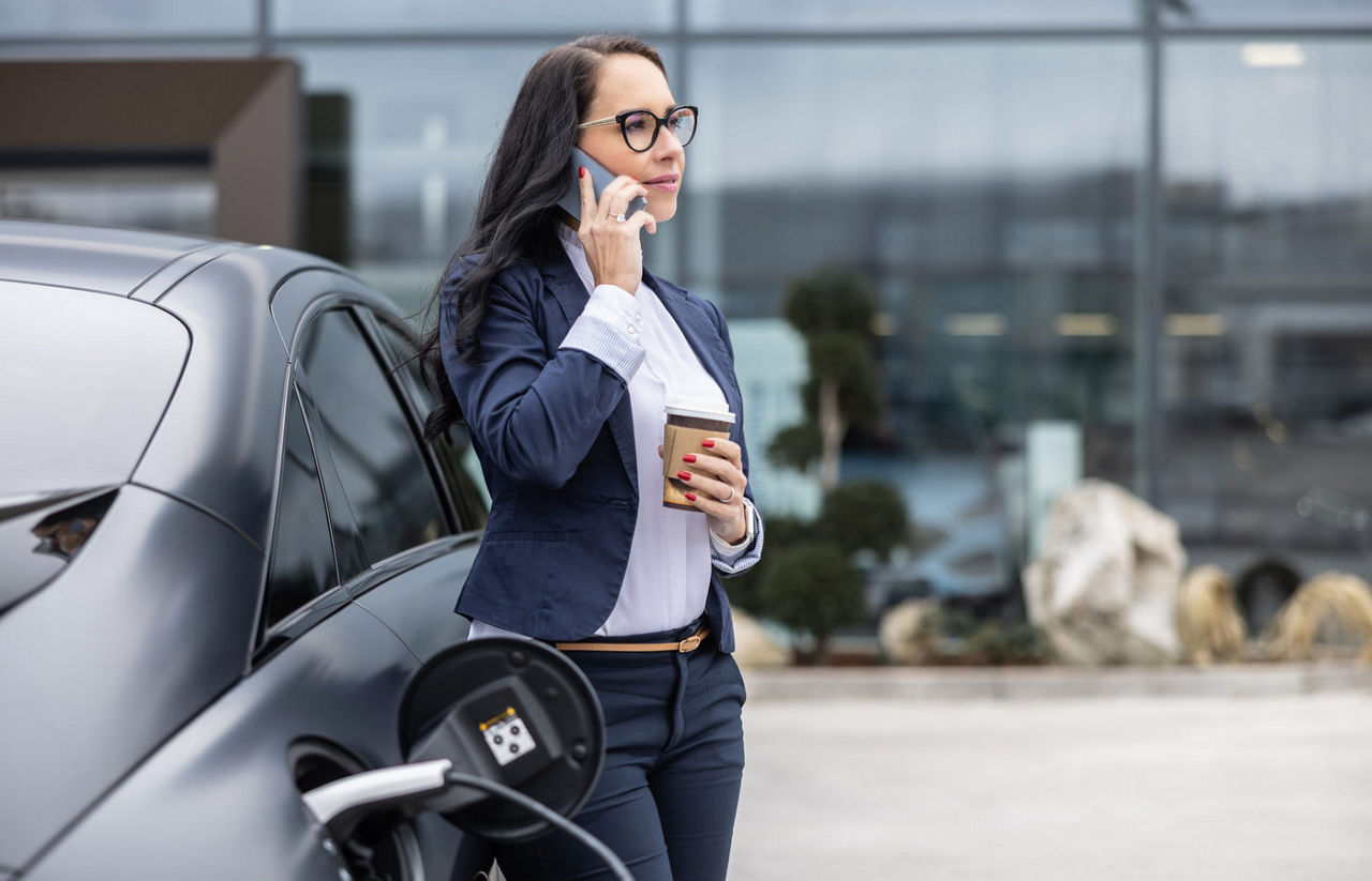 woman charging her EV while talking on the phone