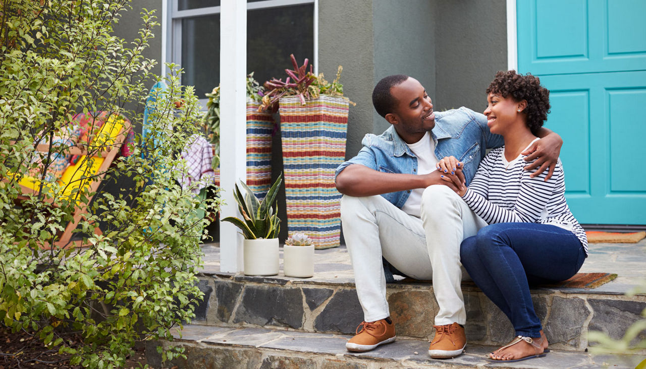 Young couple sit looking at each other outside their house