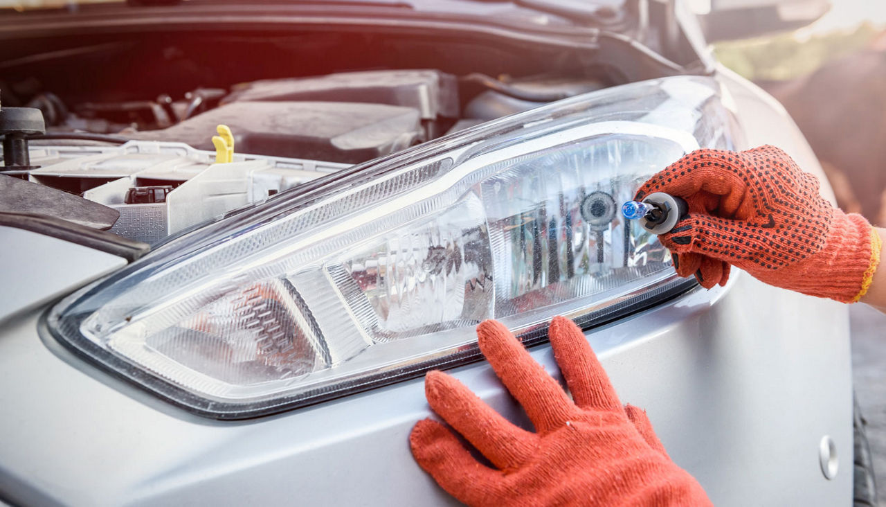 hand holding headlight bulb in front of car headlight