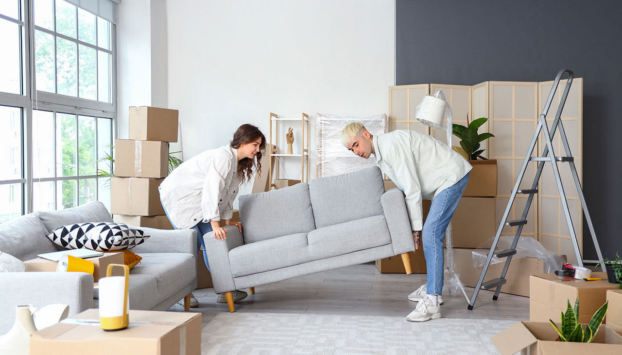 Young couple carrying sofa in room on moving day