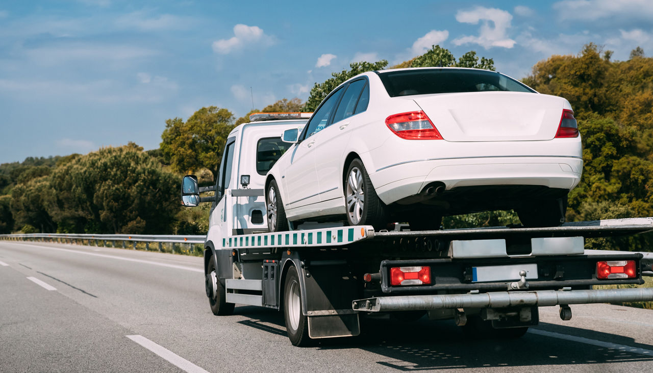 Tow truck transporting white car after running out of gas