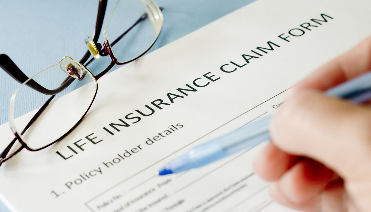 Closeup of a person holding a pen about to sign a life insurance claim form