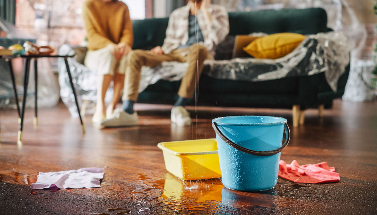 A living room where several buckets are catching are catching leaks from the ceiling