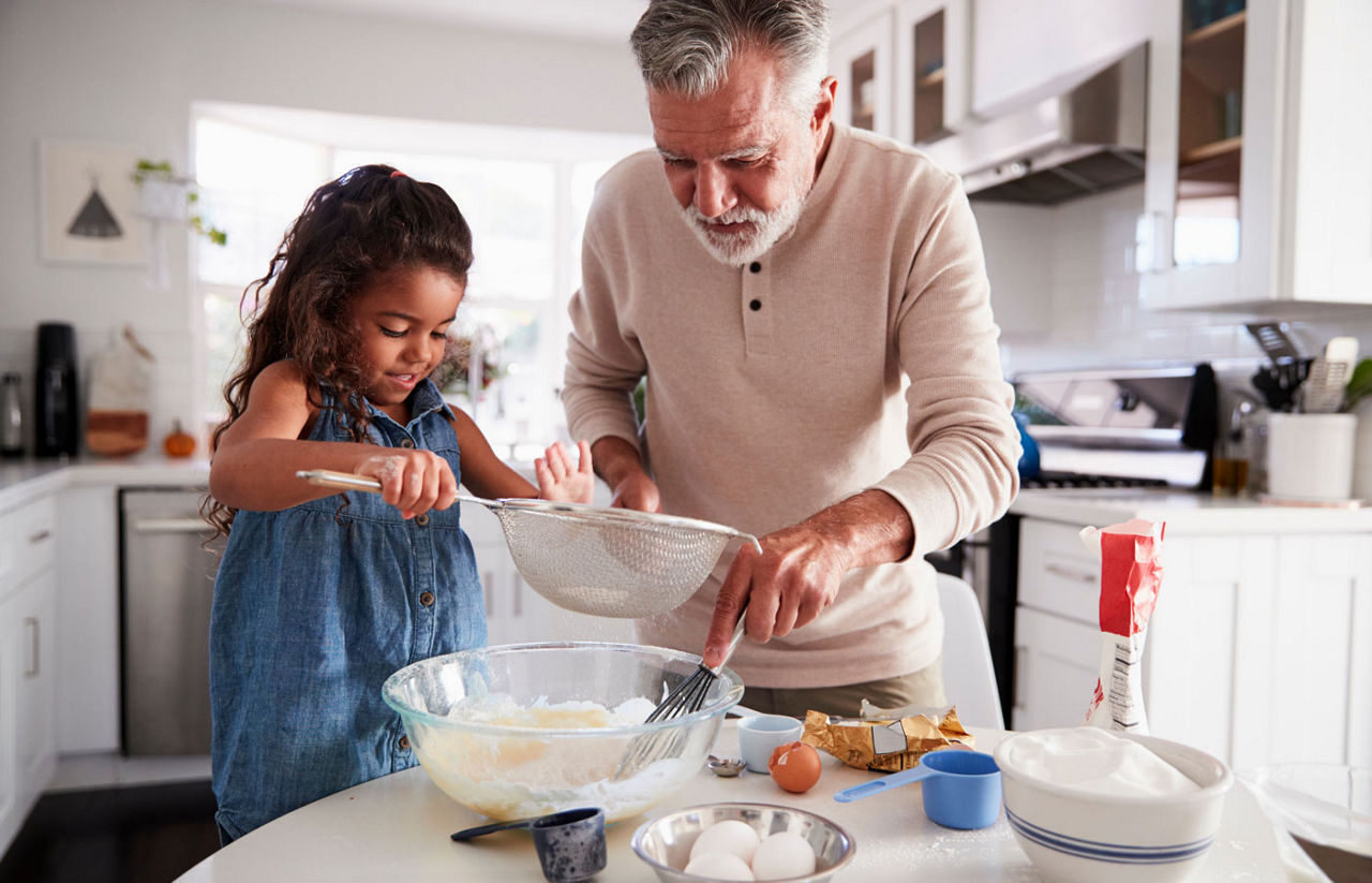 Young girl preparing cake mixture with her grandfather at the kitchen table