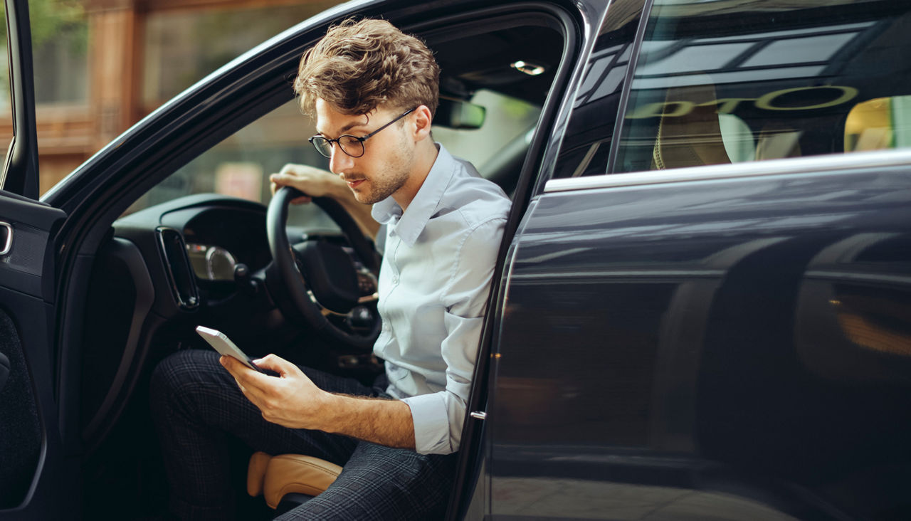 man looking at his phone sitting in car