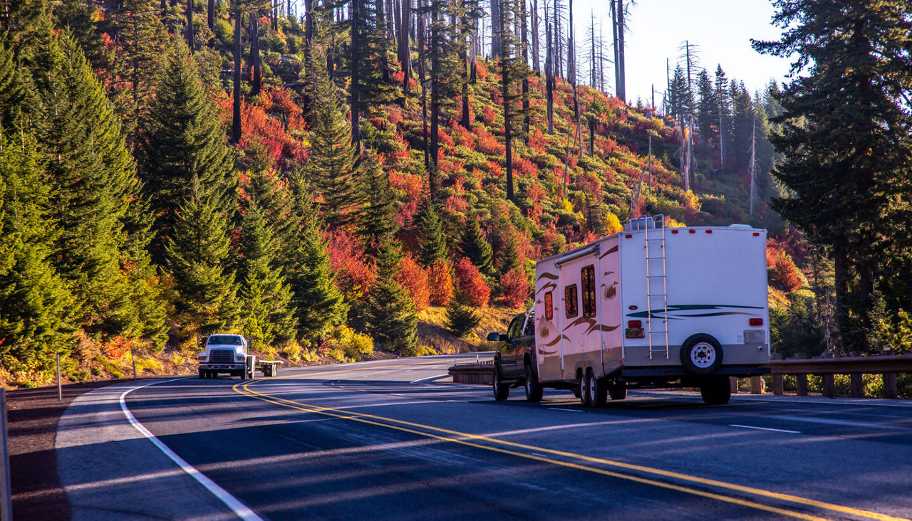 A recreation vehicle drives through fall color foliage along highway