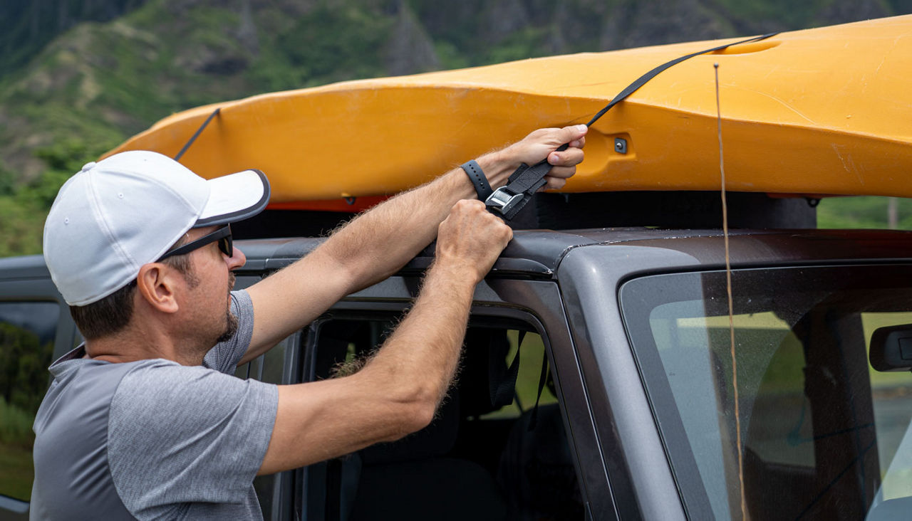 Man loading and securing kayak on top of car