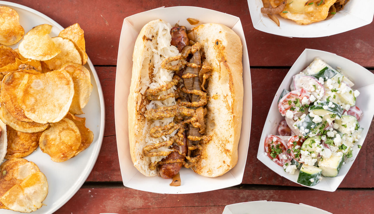 Hot dog with sauerkraut, grilled onions, and mustard, chips and a salad
