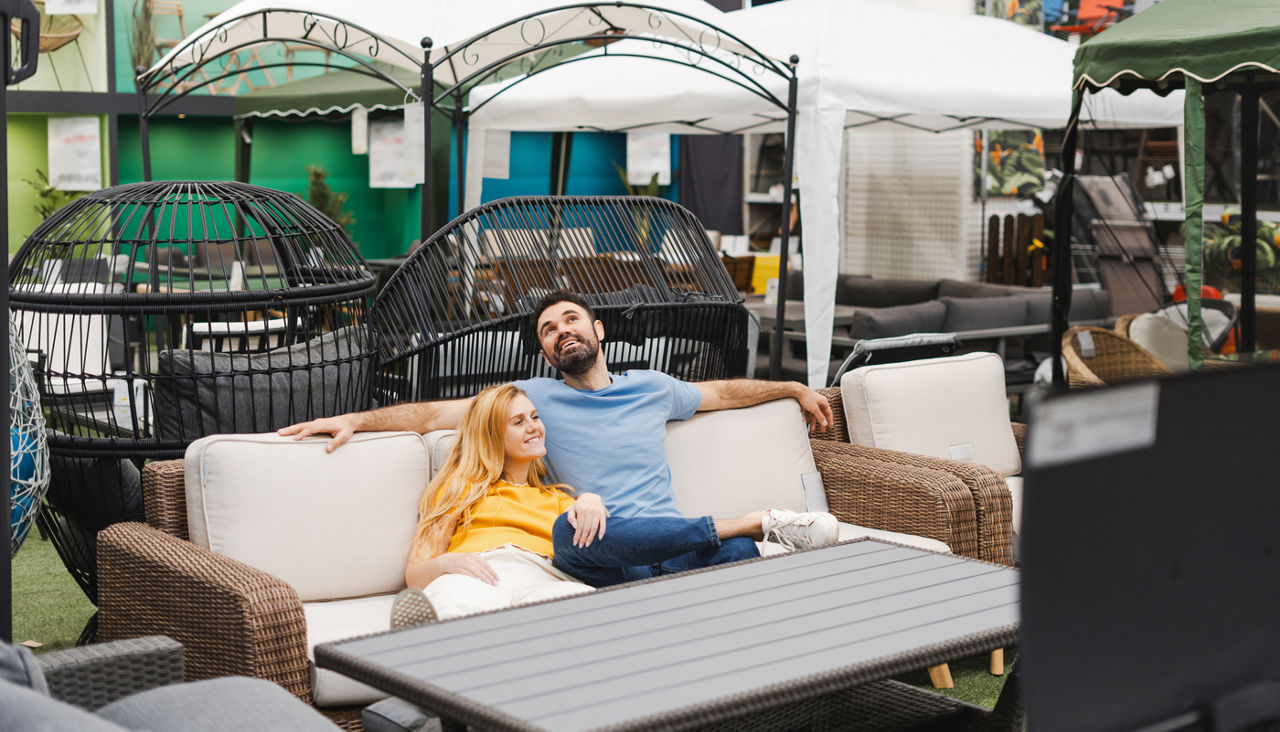 Happy young couple sitting on an outdoor sofa in the furniture department of store