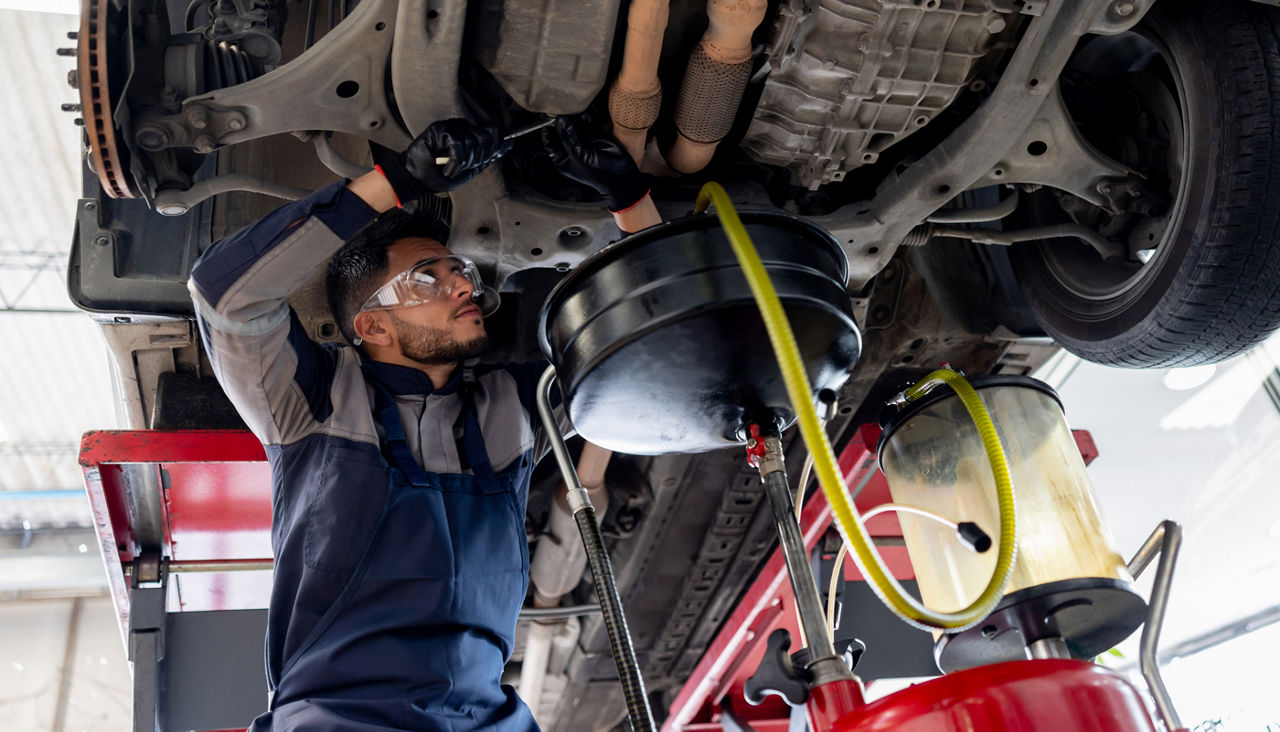 Mechanic working underneath car lifted in a shop changing fluids