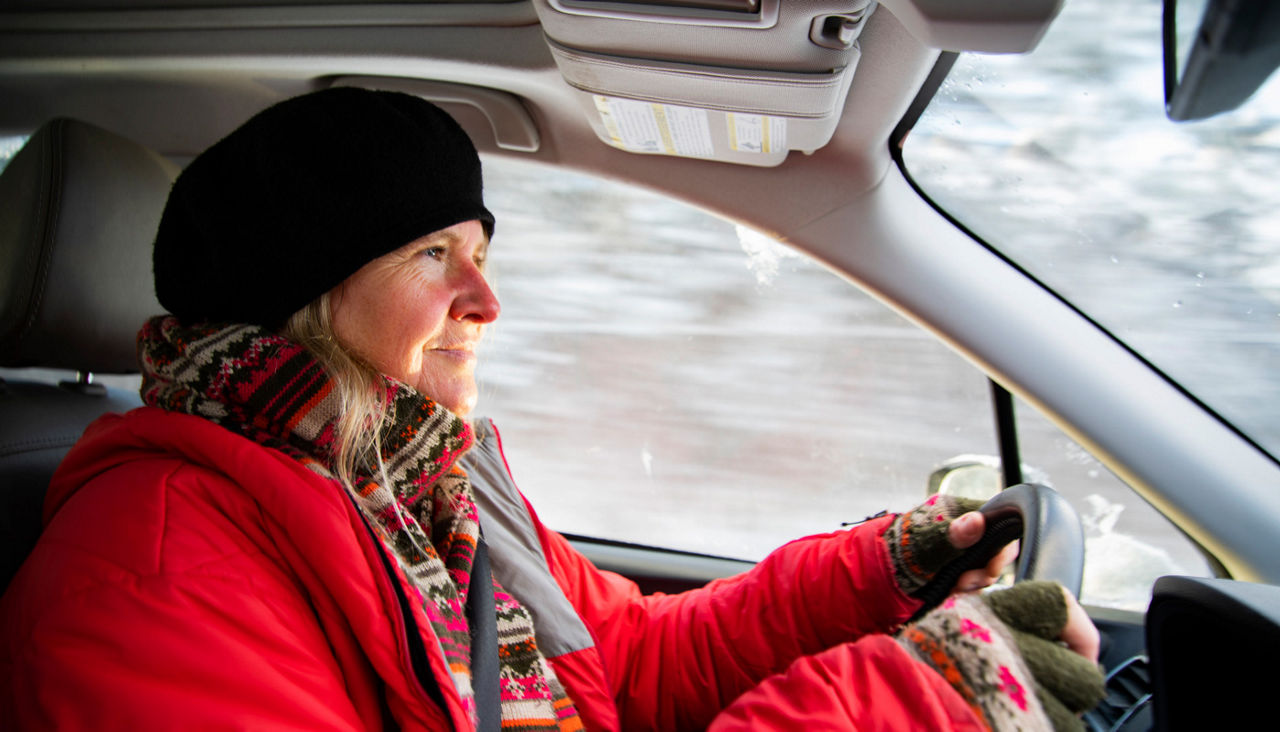 A woman driving her car on bright snowy winter day.
