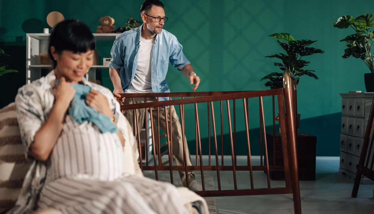 Father bringing baby crib to pregnant wife in nursery