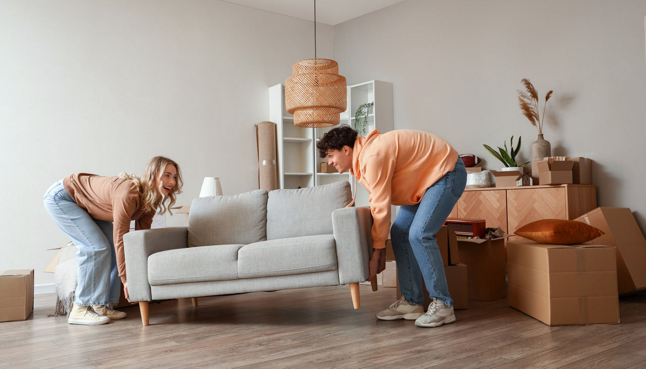 Young couple carrying sofa in room on moving day