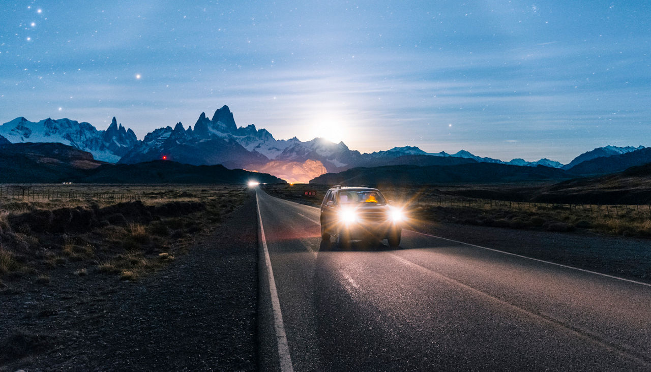 Car driving at night on a dark road with mountains behind