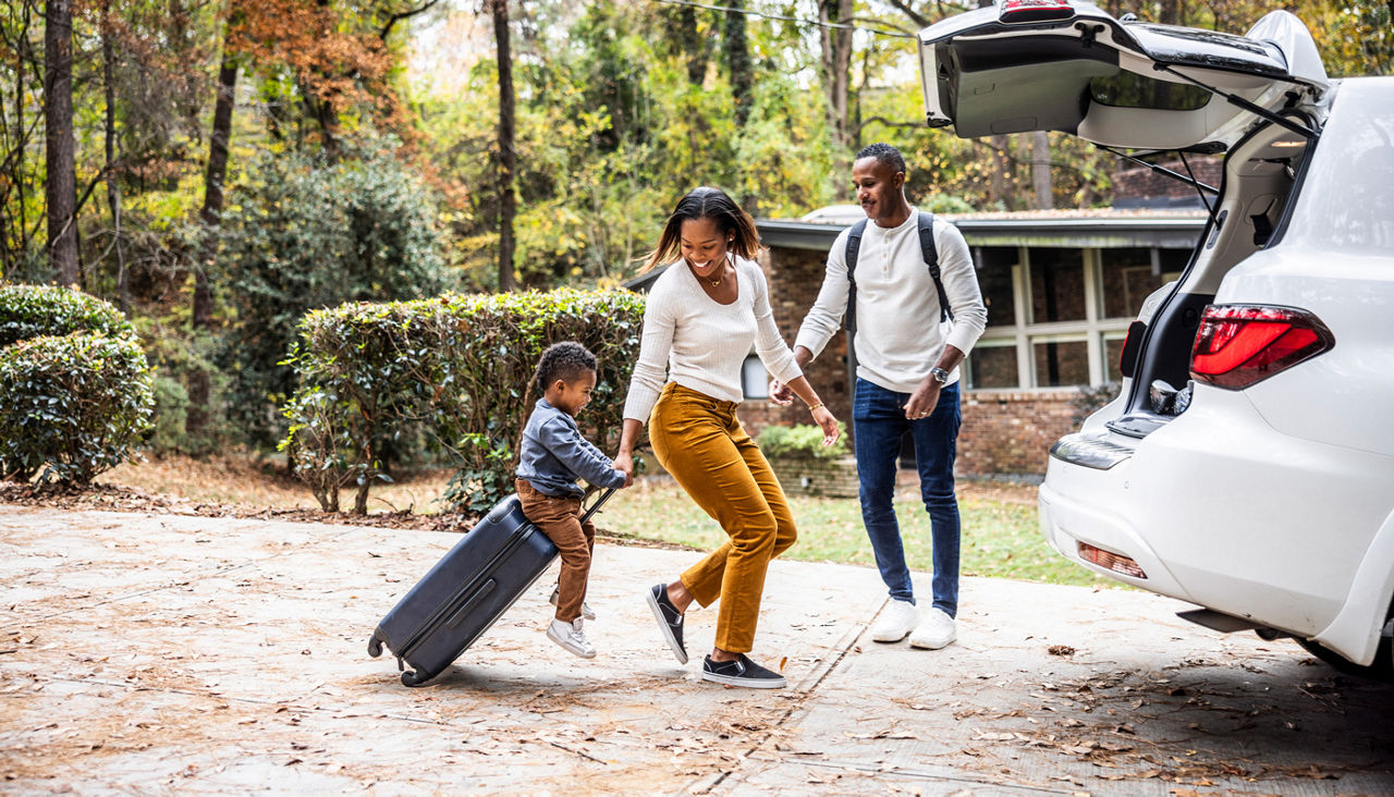 Mother pulling young boy on suitcase and loading car for family vacation