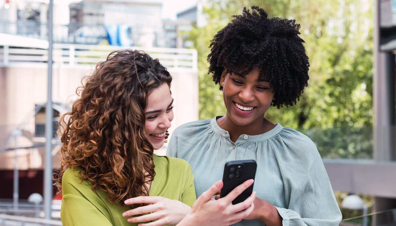 Two young adult women smile as they look at a cell phone