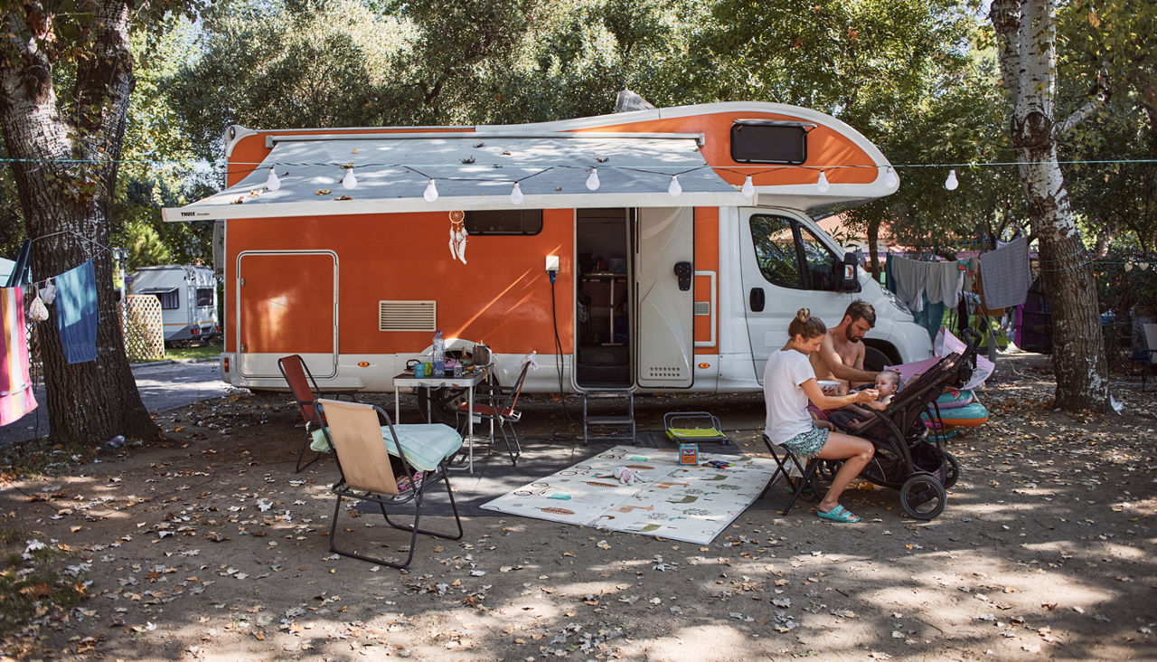Happy family feeding twin babies by the camper trailer in nature