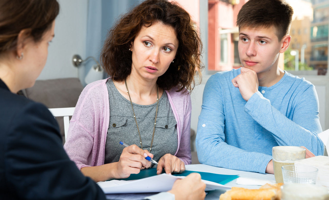 Woman with teenage son and insurance agent sitting at table and signing paperwork