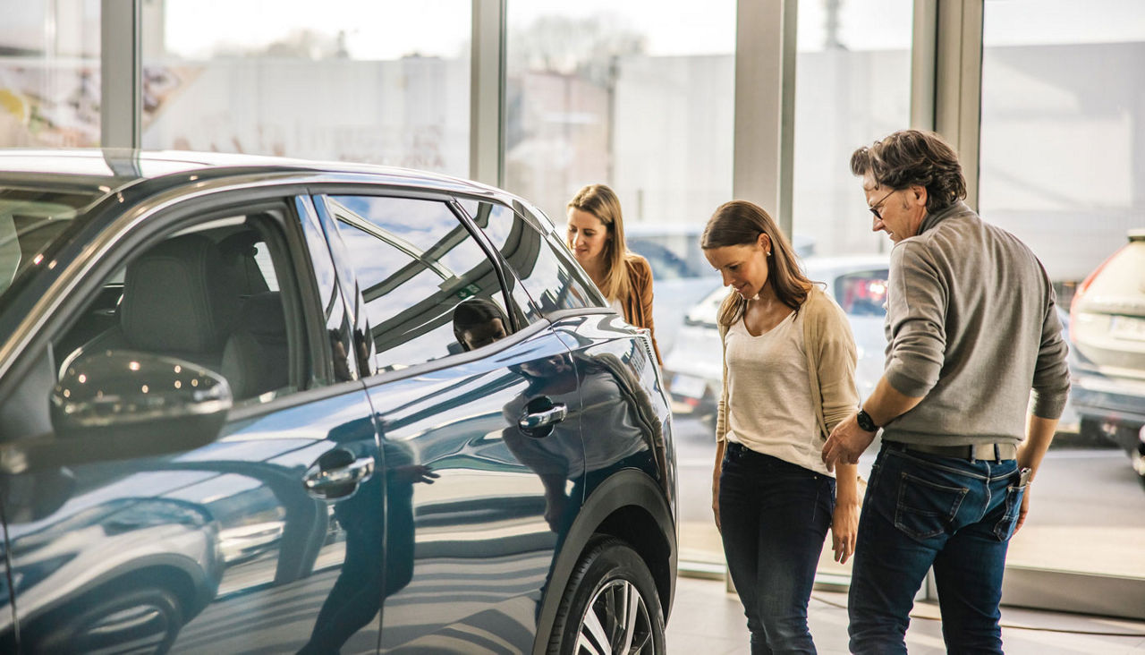 Family of three looking at the car trunk of a new SUV in the evening indoors at a car dealership