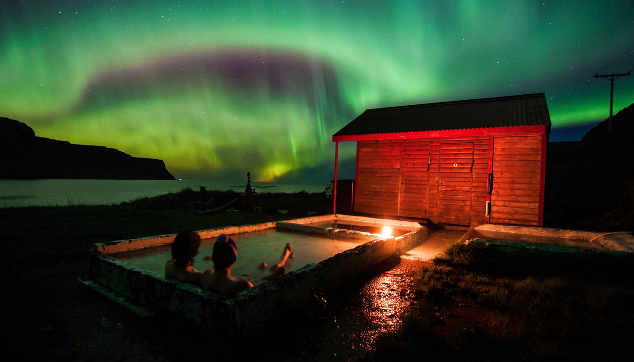 Relaxing in geothermal hot pool under northen lights (Aurora Borealis) in Iceland