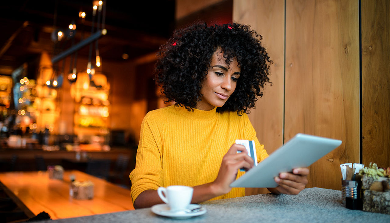 Woman sits at table holding credit card and tablet