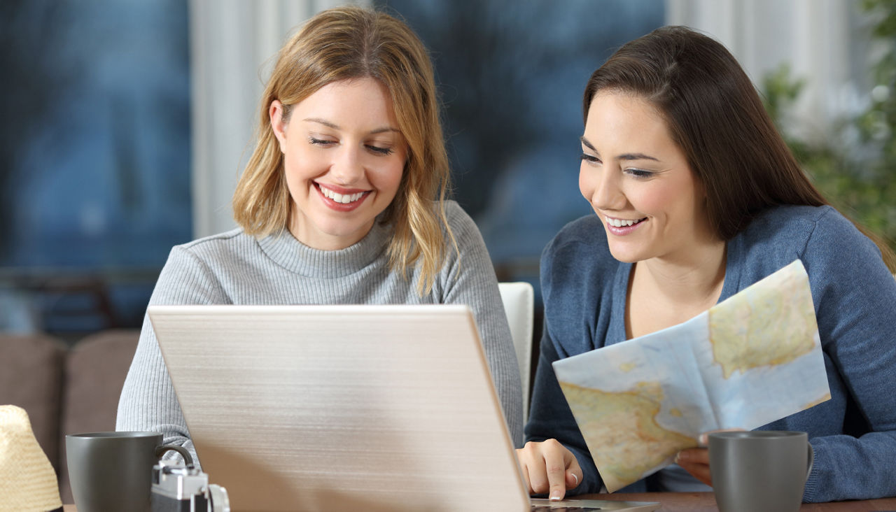 Two women planning trip using laptop