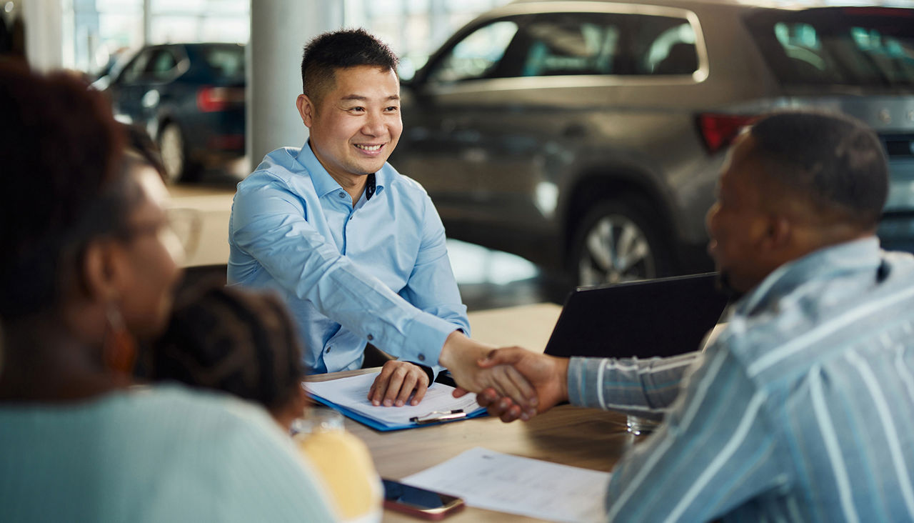 Happy car salesman came to a successful agreement with black family during a meeting in a showroom.