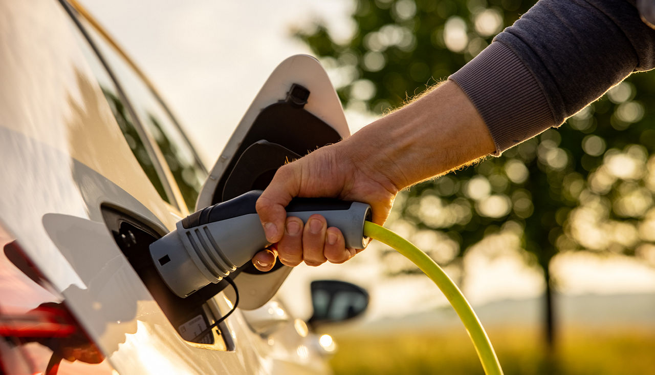 A hand connects an electric vehicle to a charging station. 