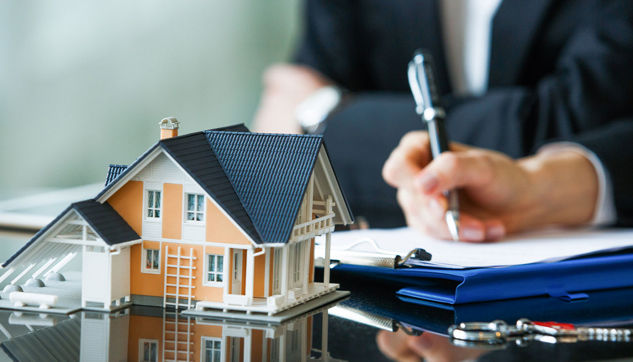 : Someone signs a form next to a small model home on the table. 