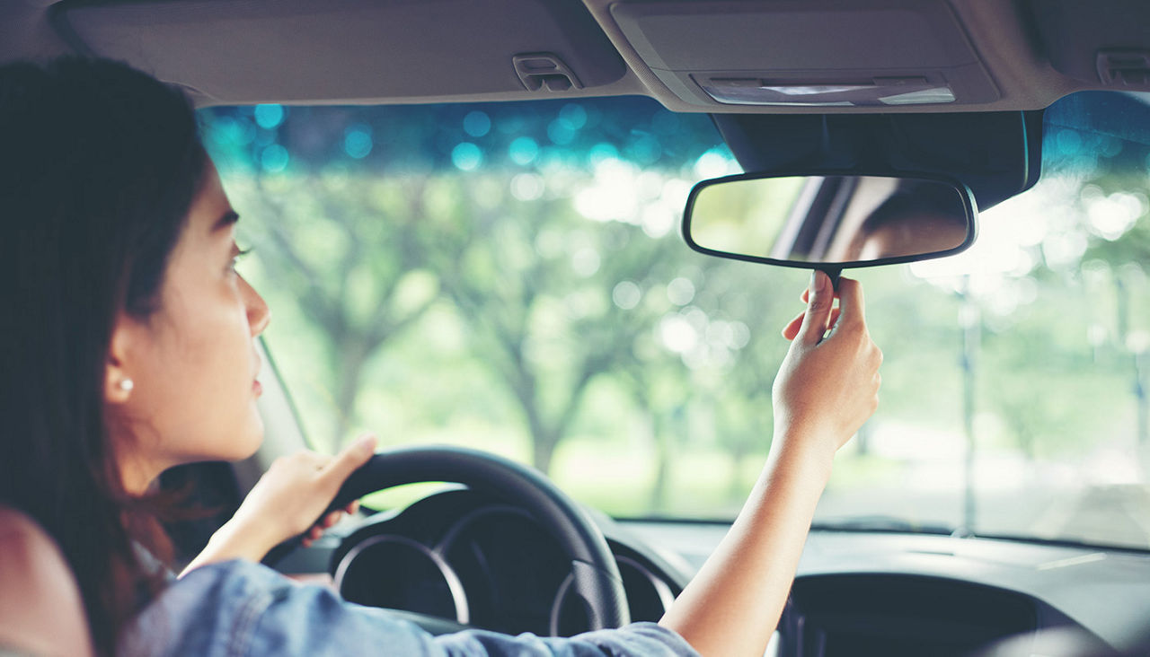 A woman adjusts a rearview mirror.