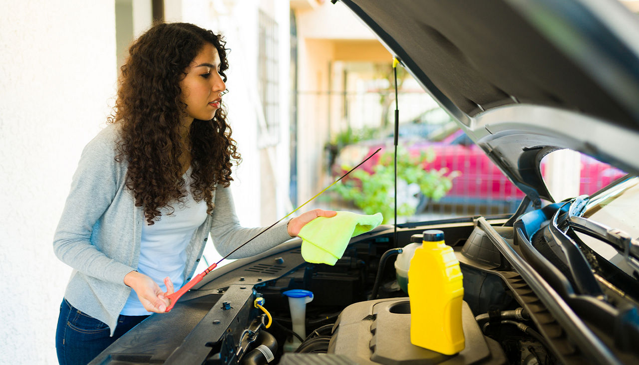 A woman wipes a dipstick with a cloth as she checks the oil level of a vehicle.