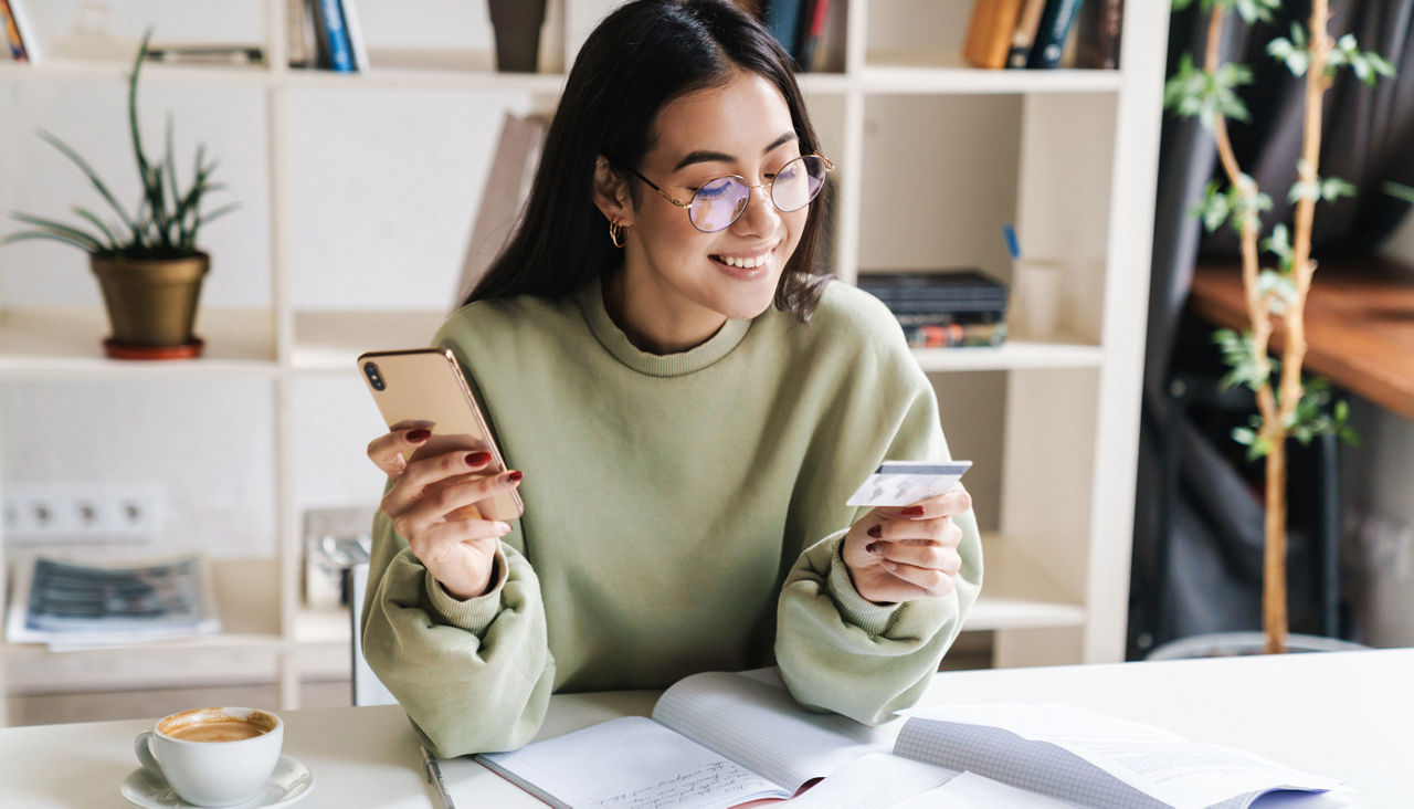 Happy optimistic young girl student holding credit card with cell phone