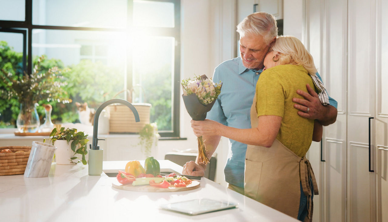 Senior couple cooking in the kitchen with flowers in hand