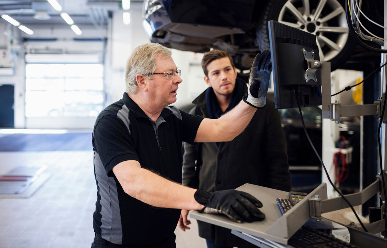 Senior mechanic showing computer monitor while discussing with customer at repair shop