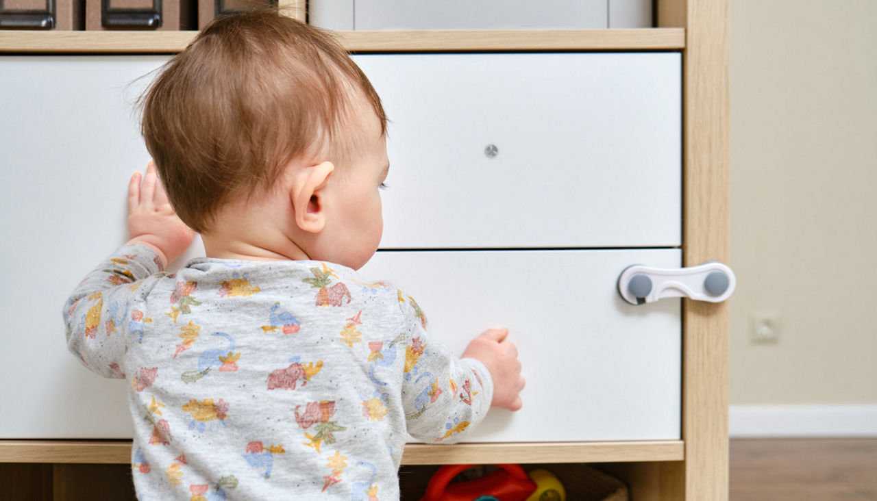 Small baby trying to open a drawer with a child  proof lock