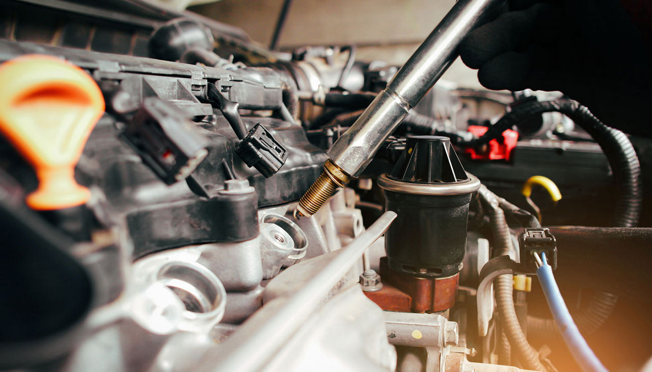 A auto mechanic is installing automobile iridium spark plugs into the ignition spark socket of the engine block in the engine compartment with a specific tools