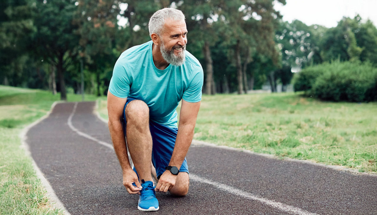 active mature or middle aged senior man fixing shoelace on his running shoe after exercising outdoors