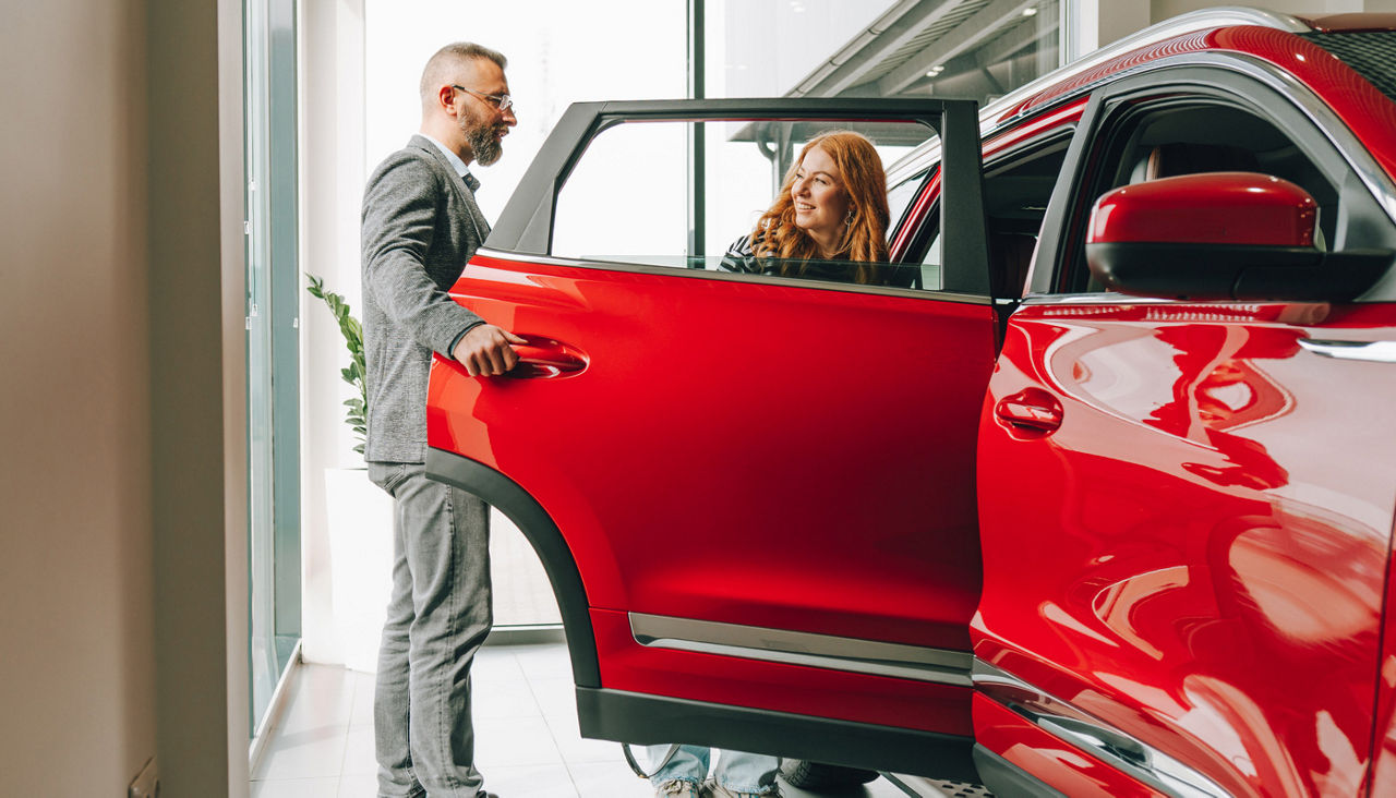 Man opening the door for a young woman at a car dealership
